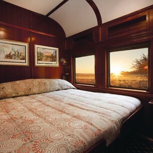 Der Innenraum eines Luxuszugs mit Doppelbett und Blick nach draußen in die Natur.
