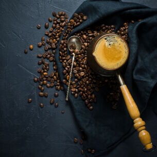 Geröstete Bohnen und frisch gebrühter Kaffee auf einem dunklen Tuch angerichtet