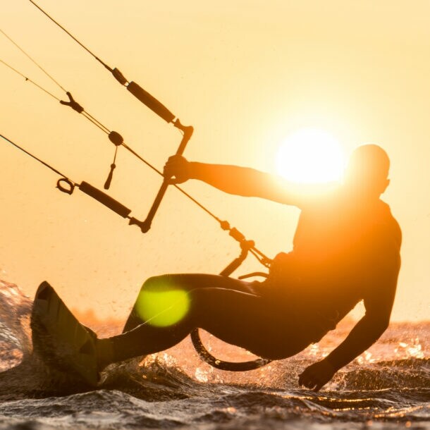 Silhouette des Kitesurfers, der bei schönem Sonnenuntergang mit Sonne neben dem Fahrerkopf reitet