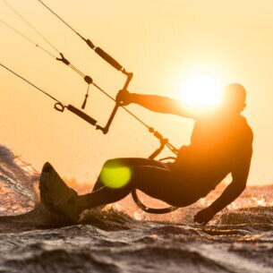 Silhouette des Kitesurfers, der bei schönem Sonnenuntergang mit Sonne neben dem Fahrerkopf reitet