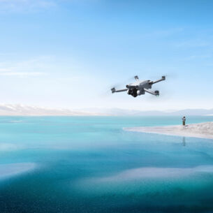 Drohne DJI Mini 3 Pro wird von einer Person in weiter Entfernung über einen kristallblauen See geflogen