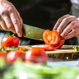 Hand mit Messer schneidet Tomaten
