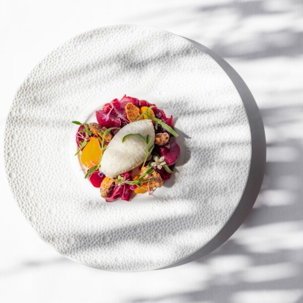 Ein elegant drapiertes Sternegericht aus Rote Bete und Mousse von Ziegenkäse auf einem weißen großem Teller.