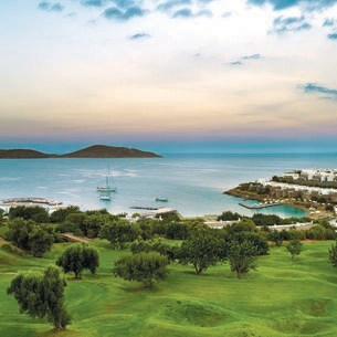 Panorama eines hügeligen Golfplatzes mit Hotelanlage am Meer