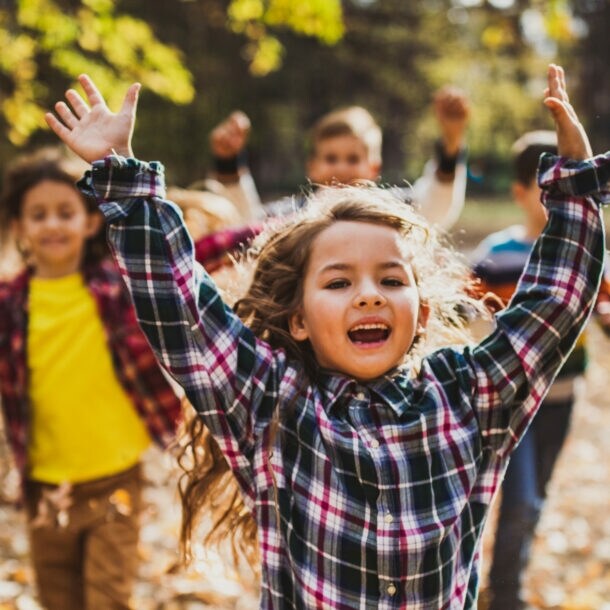 Vier fröhliche Kinder rennen im Freien durchs Laub