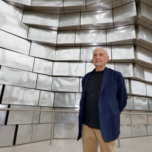 Architekt Frank Gehry vor einer Fassade aus glänzenden Aluminiumplatten