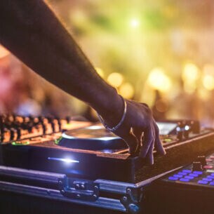Die Hand eines DJs am Mischpult auf einem Festival mit Menschenmenge im Hintergrund
