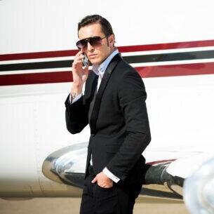 Junger Geschäftsmann neben dem Privatjet-Flugzeug, der mit seinem Smartphone telefoniert.