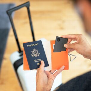 Eine Person hält einen Reisepass und einen Schlüsselfinder in der Hand