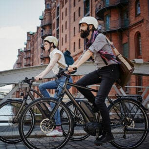 Ein Mann und eine Frau mit Fahrradhelmen fahren auf E-Bikes durch die Hamburger Speicherstadt.