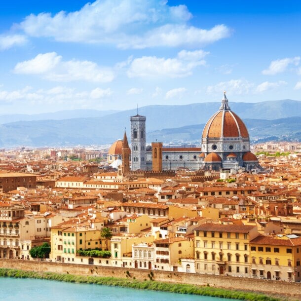 Blick auf eine mediterrane Stadt am Fluss mit historischen Gebäuden und einer Kathedrale