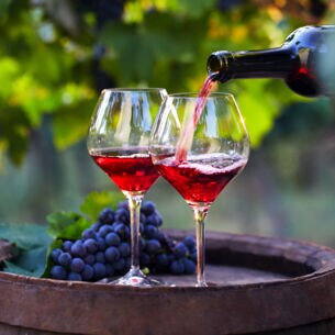 Zwei Weingläser mit hellem Rotwein auf einem Holzfass