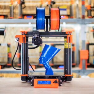 Ein 3D-Drucker mit Filament-Spulen und einer kleinen, gedruckten Nofretete-Büste aus blauem Kunststoff