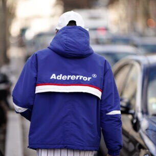 Rückansicht eines Mannes auf einer Straße mit blauer Trainingsjacke mit dem Markennamen Adererror