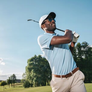 Porträt eines dunkelhäutigen Golfers in einem blauen Poloshirt beim Abschlag auf einem Golfplatz
