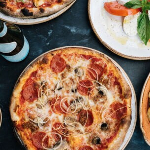 Aufsicht einer Pizza neben weiteren italienischen Gerichten und einem Glas Wein auf einem Tisch