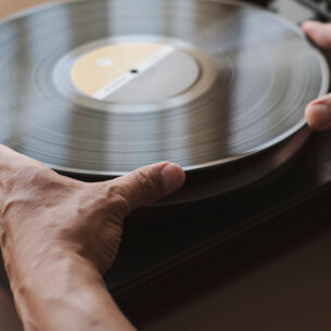 Zwei Hände, die das Vinyl auf dem Plattenteller aufnehmen