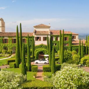 Ein begrüntes, luxuriöses Herrenhaus im französischen Stil, umgeben von einem Garten mit Zypressen