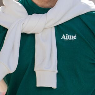 Oberkörper eines sportlichen Mannes in einem grünen T-Shirt mit dem Schriftzug der Marke Aimé