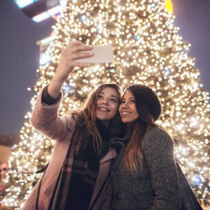 Zwei Freundinnen machen ein Selfie vor einem erleuchteten Weihnachtsbaum