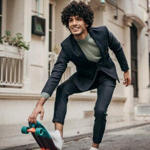 Ein junger Mann mit Anzug und Sneakern auf einem Skateboard in der Stadt