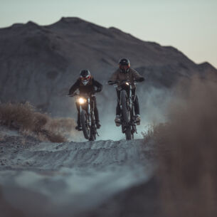 Zwei Motorradfahrer fahren in der Dämmerung durch eine Wüstenlandschaft