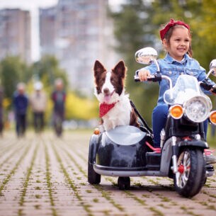 Kleines Mädchen mit Hund auf einem Kindermotorrad