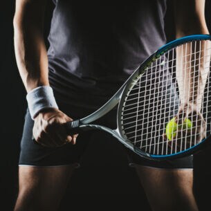 Eine Person hält einen Tennisschläger und Tennisball in der Hand.