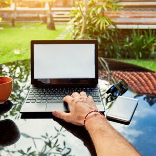 Blick auf einen Laptop, der auf einem Tisch in einem tropischen Garten steht.