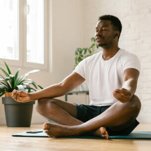 Ein Mann sitzt im Schneidersitz auf einer Yogamatte und meditiert mit einer Meditations-App