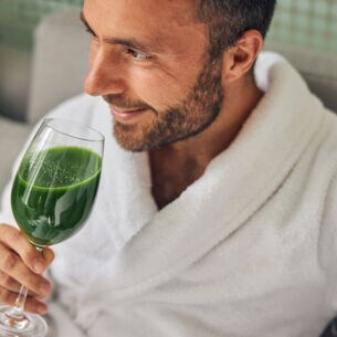 Mann in Bademantel, der ein Glas mit grünem Inhalt in der Hand hält