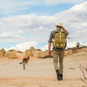 Rückansicht eines Mannes mit Rucksack, der durch eine Wüstenlandschaft mit Kängurus im Outback Australiens wandert