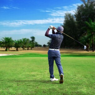 Ein Golfspieler von hinten auf einem Golfplatz, im Hintergrund Palmen