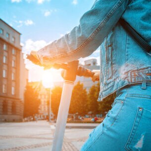 Eine Person in Jeanskleidung von hinten auf einem E-Tretroller auf einer Straße