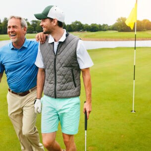 Zwei Golfspieler laufen über einen Golfplatz und lachen