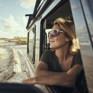 Eine lächelnde Frau mit Sonnenbrille in einem Auto am Strand