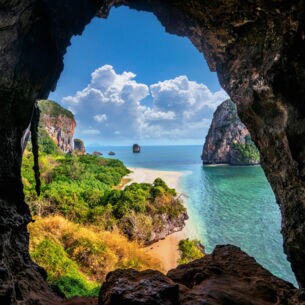 Blick aus einer Höhle auf Strand, Meer und Bäume