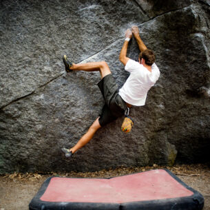 Eine Person klettert ohne Seil knapp über dem Boden an einer Felswand entlang, unter ihr liegt eine Matte
