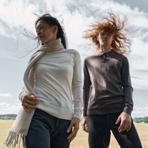 Zwei Frauen mit wehenden Haaren, die in Hose und Pullover gekleidet sind, eine mit Schal