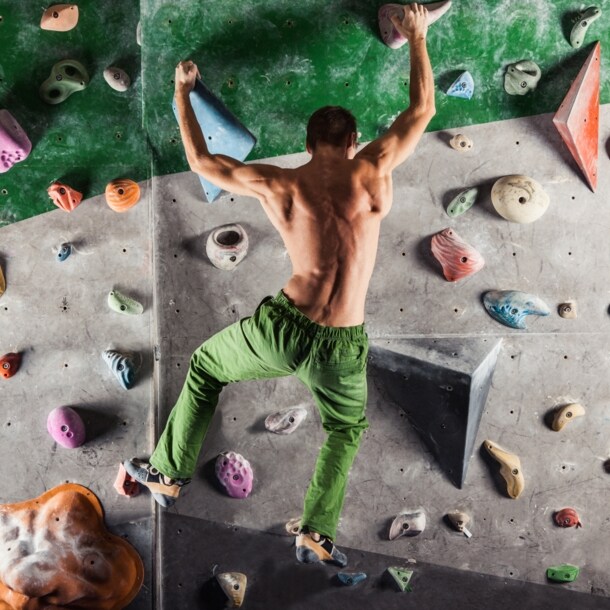Ein Mann in grüner Hose und mit nacktem Oberkörper bouldert an einer Kletterwand
