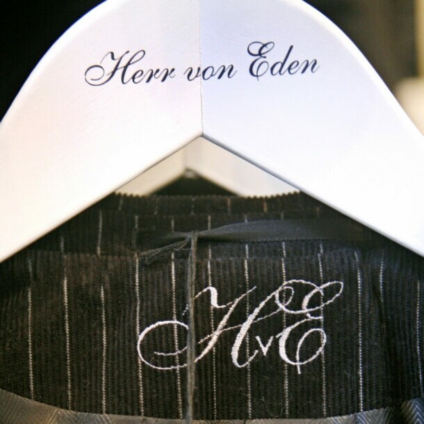 Detailaufnahme eines Nadelstreifenanzugs auf einem weißen Kleiderbügel mit einer geschnörkelten Aufschrift