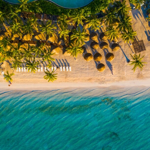 Tropischer Sandstrand mit Palmen und Badeliegen aus der Vogelperspektive