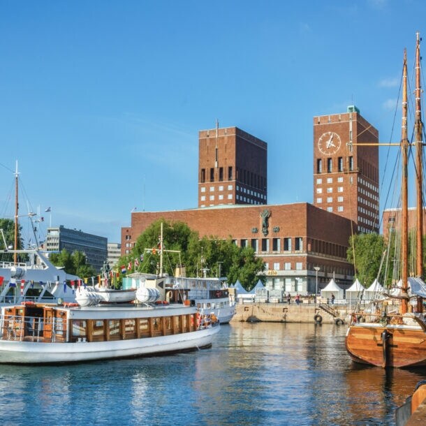 Blick auf das rote Rathaus von Oslo mit Backsteintürmen vom Wasser aus, im Vordergrund Segelboote