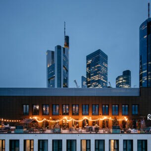 Eine beleuchtete Rooftop-Bar vor der Frankfurter Skyline bei Nacht