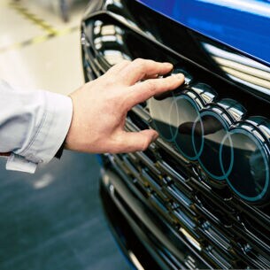 Eine Hand berührt die Audi-Ringe an einem Pkw.