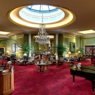 Elegante Hotellobby mit Kronleuchter und rotem Teppichboden, auf dem sich ein Piano und Sitzgelegenheiten befinden