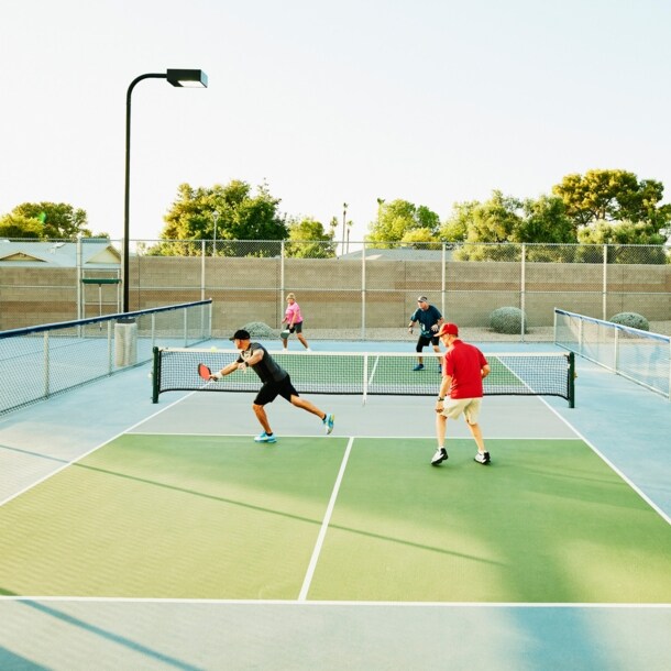 Vier Spieler bei einem Pickleball-Match auf einem Tennishartplatz unter freiem Himmel