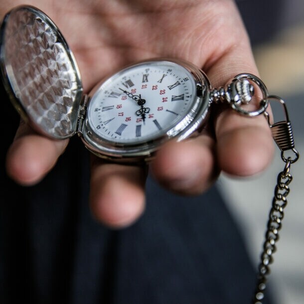 Eine Person hält eine aufgeklappte Taschenuhr in der Hand