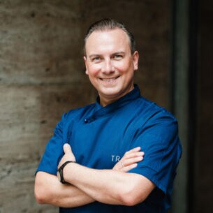 Lächelndes Porträt von Tim Raue in einer blauen Kochjacke