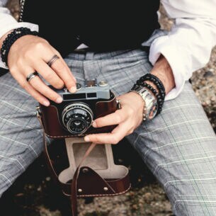 Eine Person sitzt auf einem Stein und hält eine analoge Kamera in den Händen